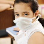 Schoolgirl with medicine mask on face, in classroom, against: virus, ill, epidemic, plague, flu